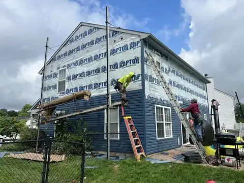 Siding replacement in progress with exposed house wrap and ladders