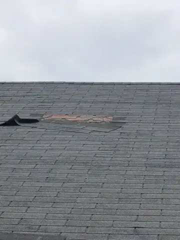 Missing shingles and exposed roof surface before repair